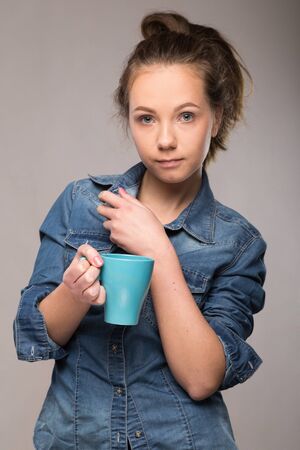 sleepy student with a cup of coffee in hand on studio backgroundの写真素材