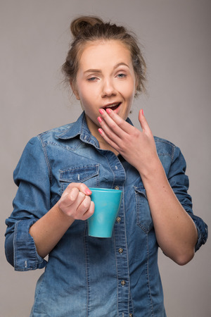 sleepy student with a cup of coffee in hand on studio backgroundの写真素材