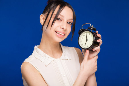 smiling young  woman with an alarm clock on a blue backgroundの写真素材