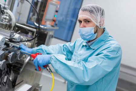 caucasian scientist in blue lab uniform configure manufacture machine with shafts and control panel,...