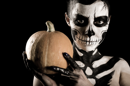 Isolated on black, closeup picture, young brunette caucasian pretty woman with scull body art with a pumpkin in hands, grey eyes, look at camera, wide opened eyesの写真素材