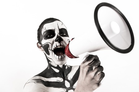 Isolated on white, closeup picture, young brunette caucasian pretty woman with scull body art holds a megaphone, grey eyes, look at camera, screams at itの写真素材