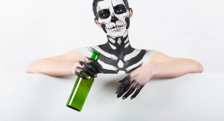 Isolated on white, closeup picture, young brunette caucasian pretty woman with scull body art holds green beer bottle, grey eyes, look at cameraの写真素材