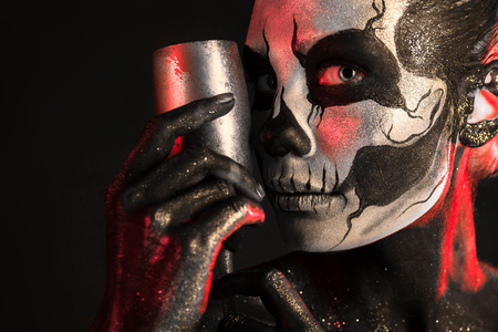 Isolated on black, closeup picture, toned red and white, beautiful young blonde caucasian woman with scull body art with wine glass in hand, grey eyesの写真素材