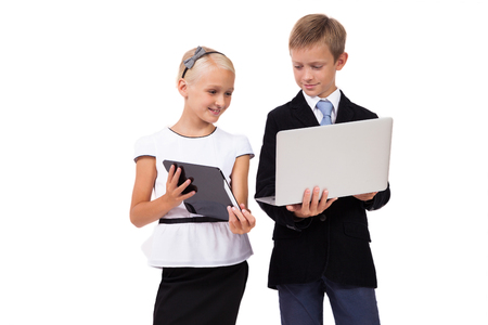schoolboy and schoolgirl with a laptop with a tablet on a white background smiling, picture with depth of field and artistic blurの写真素材