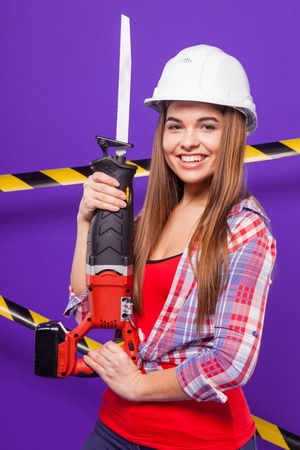 Isolated on purple, attractive sexy brunette caucasian builder girl in chechered shirt, snickers, white helmet and blue jeans stand with electro saw
Black-yellow tapeの写真素材