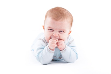 isolated on white, serious baby caucasian boy in blue pajamas lies, hands in mouthの写真素材