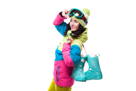 isolated on white, attractive  young caucasian woman in colorful ski suit and ski glasses hold blue ski bootsの写真素材