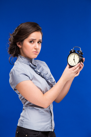 smiling young woman with an alarm clock on a blue backgroundの写真素材