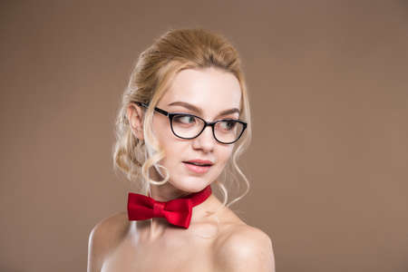 young girl in glasses with red butterfly on her neck on a beige backgroundの写真素材