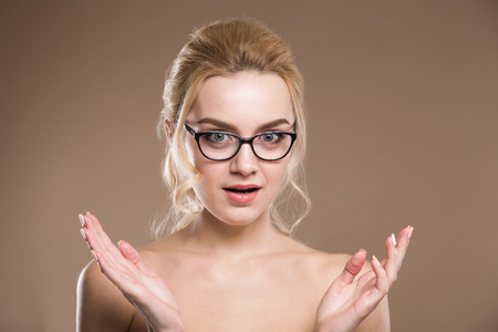 close up of surprised young lady with glasses with hands on a beige backgroundの写真素材