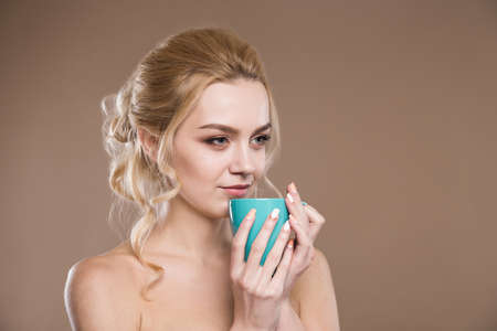 young girl with blue mug in his hands on a beige backgroundの写真素材