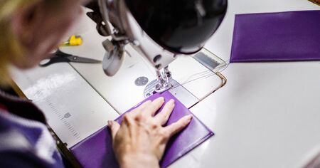 woman in uniform stitching a purple wallet with a sewing machine.の写真素材