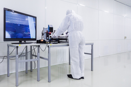 a factory worker in a white lab suit, latex gloves and face mask, working with some modern equipment during the manufacturing of a tv set.の写真素材