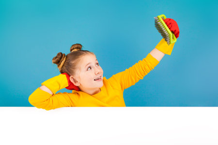 isolated on blue, adorable red-haired girl with freckles in lemon pullover and red latex gloves, holding a lime brush and looking at it. copyspace.の写真素材