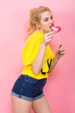 Saint Valentines Day concept. Portrait of blonde woman in yellow T-shirt and jeans shorts isolated...