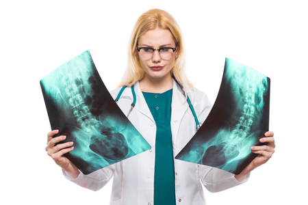 Female uncertain hesitating doctor in white coat wears stethoscope and glasses studies or compares two X-rays isolated on white background anatomy making diagnosis concept.の写真素材
