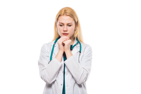 Worrying female doctor in white coat wearing stethoscope holding hands in hope for the better isolated on white background with copyspace head physician medical mistake wrong diagnosis concept.の写真素材