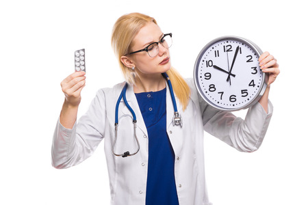 Portrait of serious female doctor in white coat and glasses with stethoscope holds pills and clock isolated on white background with copyspace time to take medicine concept.の写真素材