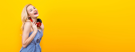 Attractive blonde cheerful smiling woman DJ with red lips in blue striped shirt on yellow background hold red headphones on her neck and have fun horizontal picture.の写真素材