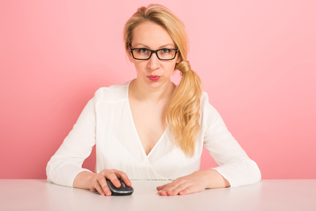 Portait of attractive businesswoman in glasses and white blouse working on computer with mouse isolated on pink background female manager working on the internet or doing shopping online concept.の写真素材