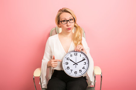 Portrait of blonde businesswoman boss in eyeglasses sitting in chair isolated on pink background...