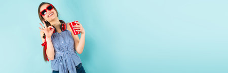 Brunette cheerful woman DJ with in striped shirt and sunglasses on blue background with copyspace...