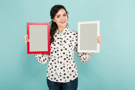 Portrait of young woman in white shirt and two frames posing on blue background with copyspace.