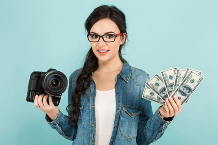 Portrait of young attractive happy woman photographer in denim and glasses shirt holding camera and...