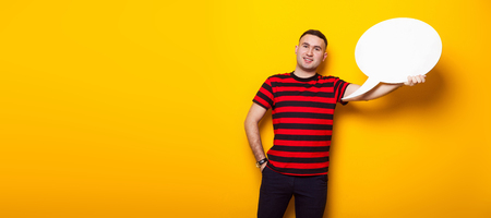 Portrait of handsome businessman in striped red T-shirt holds blank paper thinking speech bubble with empty space for your text isolated on orange background thinks of solution concept horizontal.の写真素材