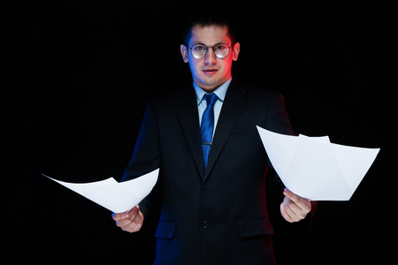 Young business man in black suit standing in office looking in camera with documents in his hands thoughtful handsome confident successful sophisticated classic smart elegant modern serious puzzled.の写真素材