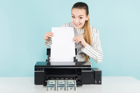 Portrait of attractive happy woman in striped shirt isolated on blue background printing dollar...