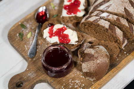 Close up view of sliced dark bread on wooden plate with sandwiches with butter and raspberry jam...