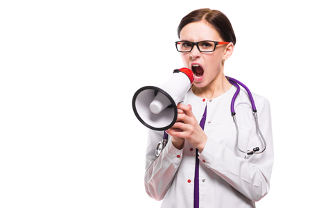 Portrait of young attractive caucasian brunette positive friendly woman doctor standingin white uniform speaking in megaphone shouting.の写真素材