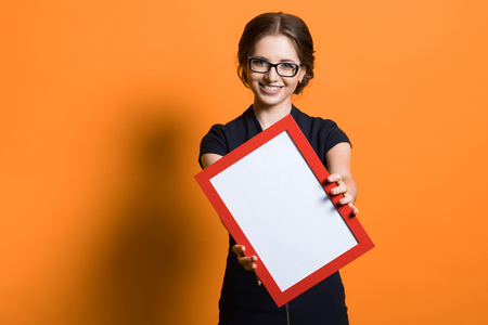 Caucasian brunette smiling attractive businesswoman in formal suit with frame in her hands standing in office looking in cameraの写真素材