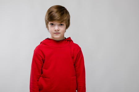 Portrait of small adorable caucasian guy in red sweater standing in studio looking in camera thinking stylish confidentの写真素材