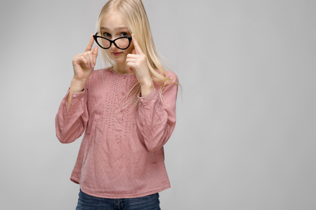 Cute naive sweet caucasian young teen girl looking in camera standing in studio holding hand on glasses sad surprised interestedの写真素材