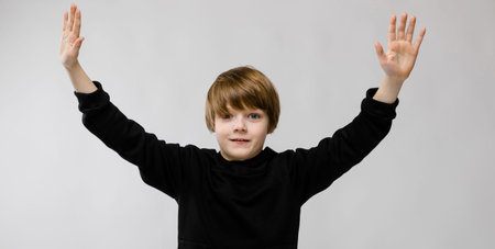 Portrait of cute little boy wearing black hoody and holding hands up like surrender isolated on grey background with copyspace childrens fashion concept.の写真素材