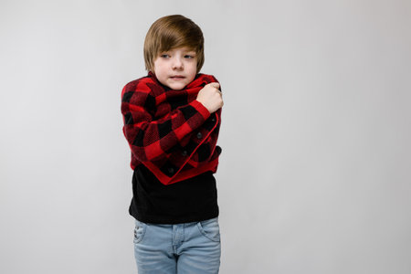 Portrait of serious little boy wearing checkered jacket and holding himself as if it is cold isolated on grey background with copyspace childrens fashion concept.の写真素材