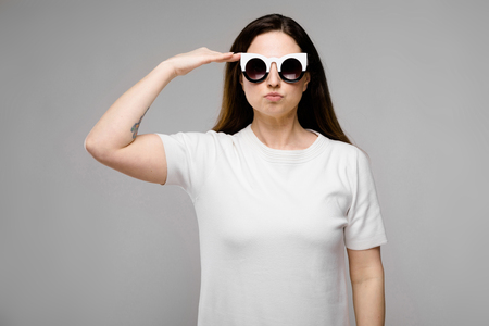 Portrait of plus size model wearing white blank T-shirt and stylish sunglasses holding her palm near head greeting isolated on grey background with copyspace fashion advertising body positive concept.の写真素材