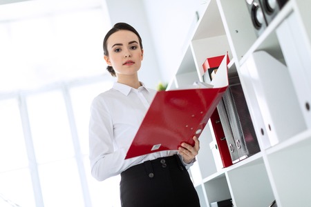 Beautiful young girl in a white blouse and black skirt. Girl with dark hair and beautiful make-up. A charming young girl is working in a bright office. photo with depth of field.の写真素材