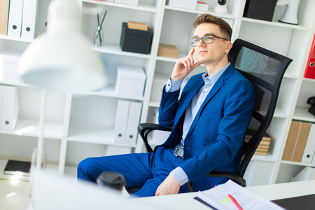 A handsome young man with glasses, a blue suit and a light shirt is working in the office. photo with depth of fieldの写真素材