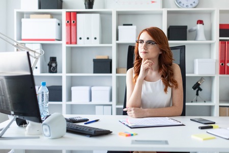 A red-haired young girl with glasses, a white blouse and a red skirt is working in the office. photo with depth of fieldの写真素材