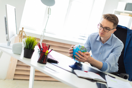 A handsome young man with glasses, blue trousers and a light shirt is working in the office. On the back of the chair hangs his jacket. photo with depth of field.の写真素材