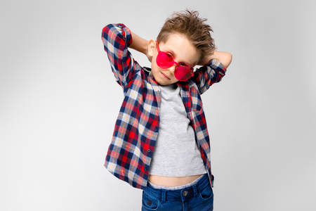 Charming happy child on gray background. The boys hair is up. The boy has a hairstyle. Boy in red sunglassesの写真素材
