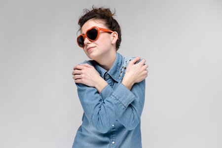 Young girl with glasses in heart on gray background. Portrait of a young beautiful girl. Charming girl in a blue denim shirt.の写真素材