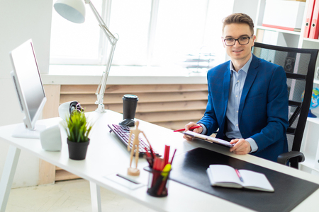 A handsome young man with glasses, a blue suit and a light shirt is working in the office. photo with depth of field.