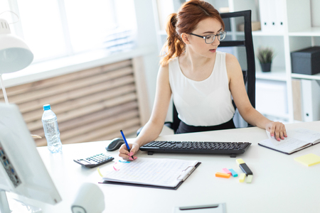 A red-haired young girl with glasses, a white blouse and a black skirt is working in the office. The hair is gathered in a bun. photo with depth of fieldの写真素材