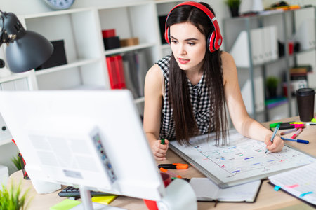 A beautiful girl in a black and white sleeveless shirt listens to music through red headphones and works in a bright office. photo with depth of fieldの写真素材