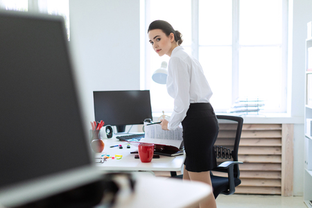 Beautiful young girl in a white blouse and black skirt. Girl with dark hair and beautiful make-up. A charming young girl is working in a bright office. photo with depth of field.の写真素材
